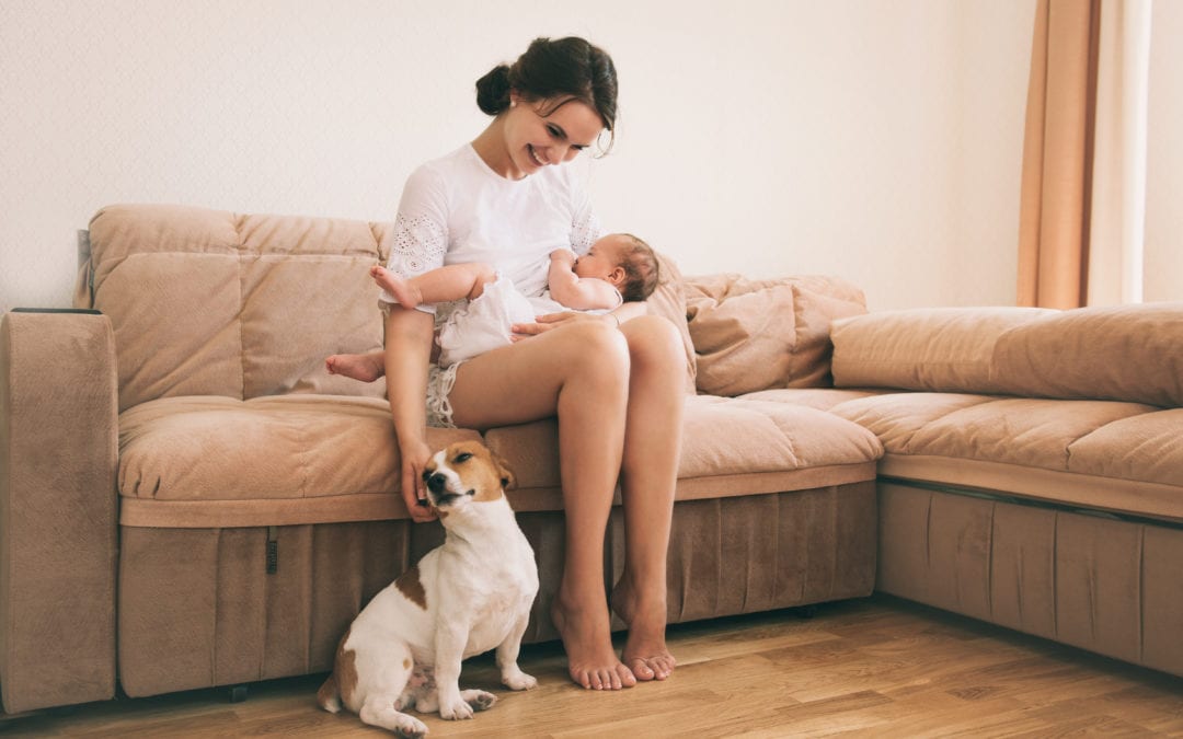 Young mom nursing and petting dog.