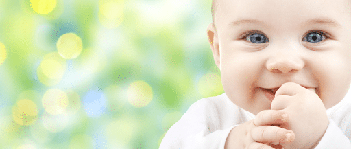 baby-smiling-while-looking-into-camera-against-green-background